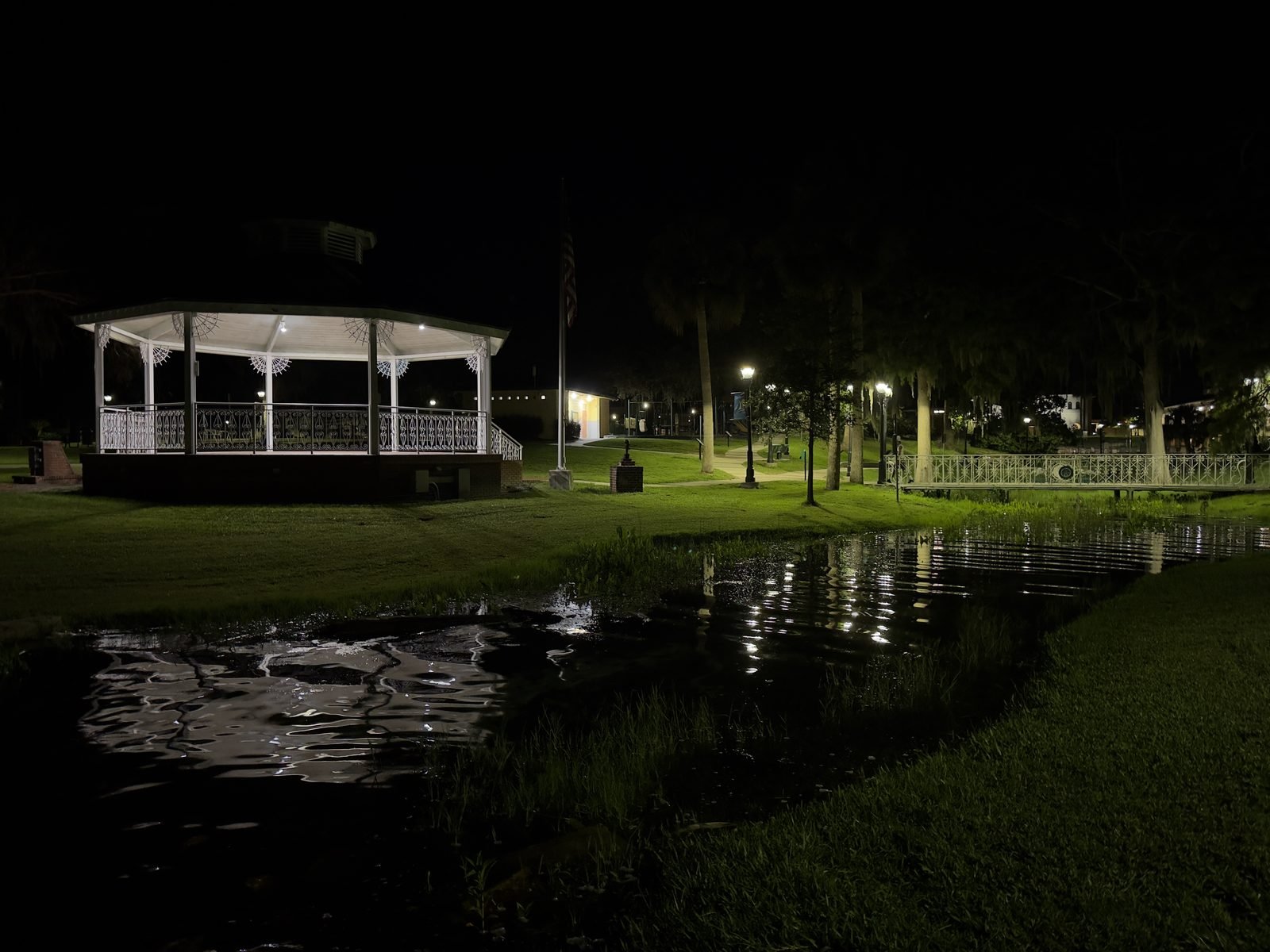 Lit gazebo and footbridge reflected in the water at a Green Cove Springs park at night