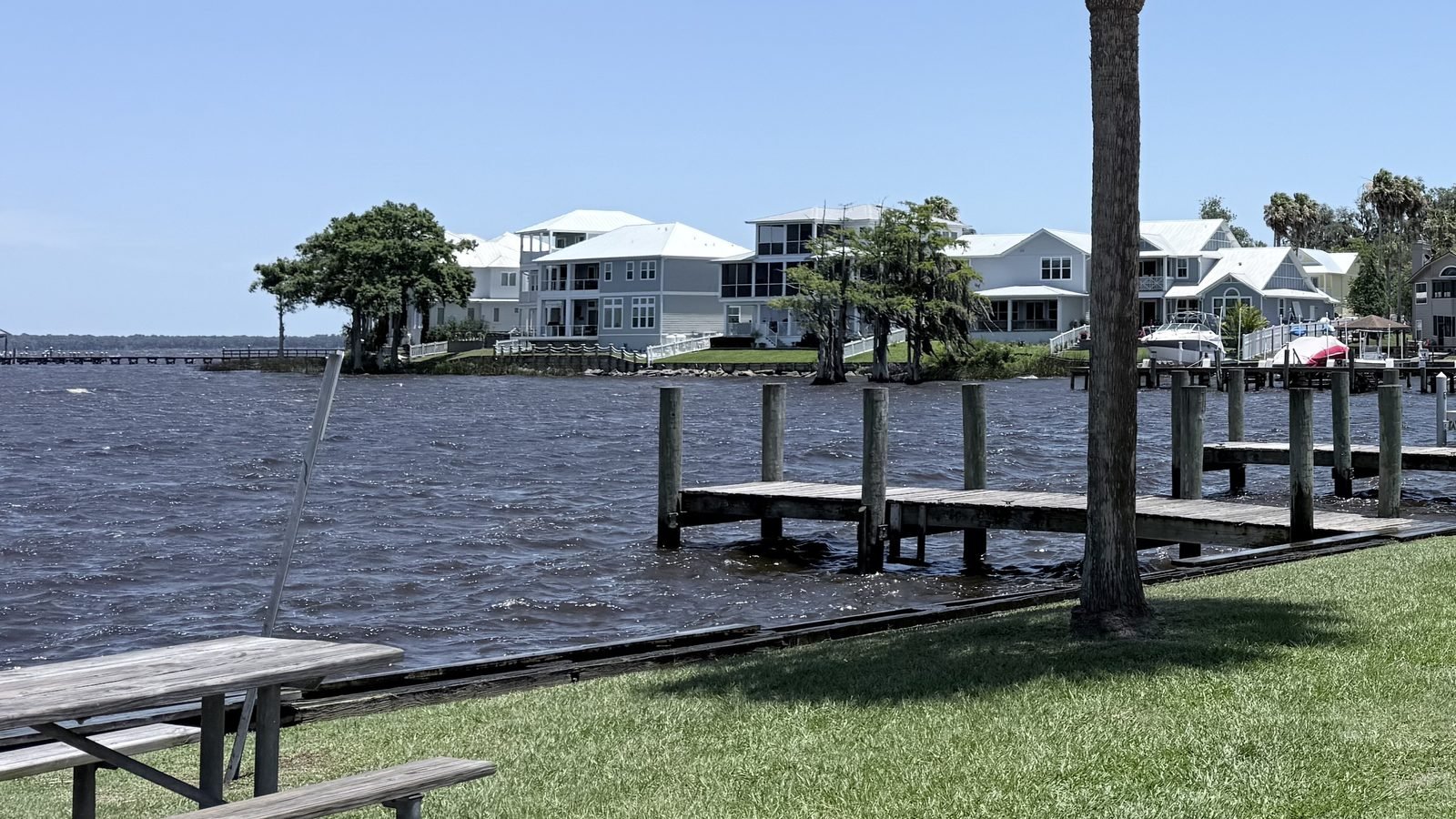 A wooden dock, palm tree and picnic table on the St. Johns River shoreline in Green Cove Springs, Clay County, Florida