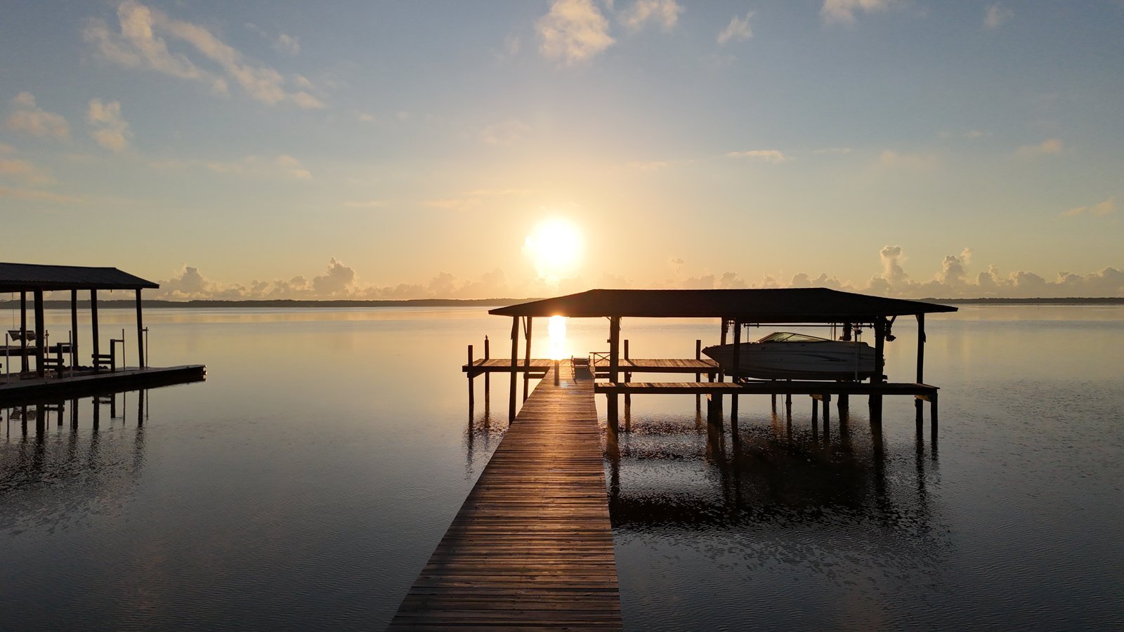 Sunset over the St. Johns River with a long wooden dock and covered boat lifts reflected in calm water.